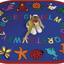 a girl sitting on a educational kids rug with letters. This rug is blue with the alphabet around the center and whimsical animals around the edge.