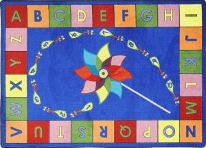 An educational kids rug with a pinwheel in the center and the alphabet around the edge.