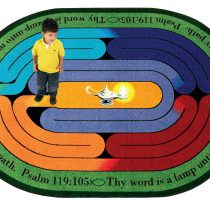 A child standing on a faith based rug that contains a maze and scripture from the bible.