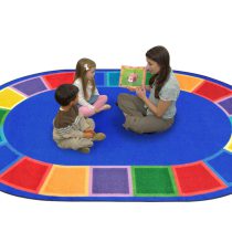 A teacher and two kids sitting on a blue oval rug with seating spaces around the edge of the rug.