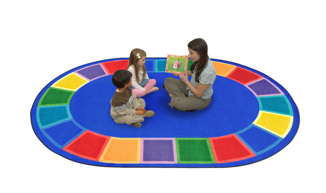 A teacher and two kids sitting on a blue oval childrens rug with seating spaces around the edge of the rug.